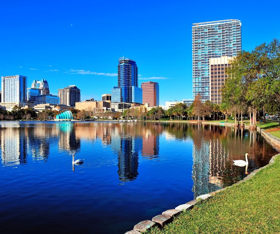 Lake Eola in Downtown Orlando with high rise building and white swans floating. One of the best places to put on your Orlando bucket list!