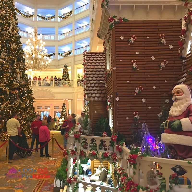 Disney Grand Floridian Gingerbread House Display with Santa on the Porch and Christmas Tree in the Background. Keep reading to learn about the best things to do at Disney World for Christmas.