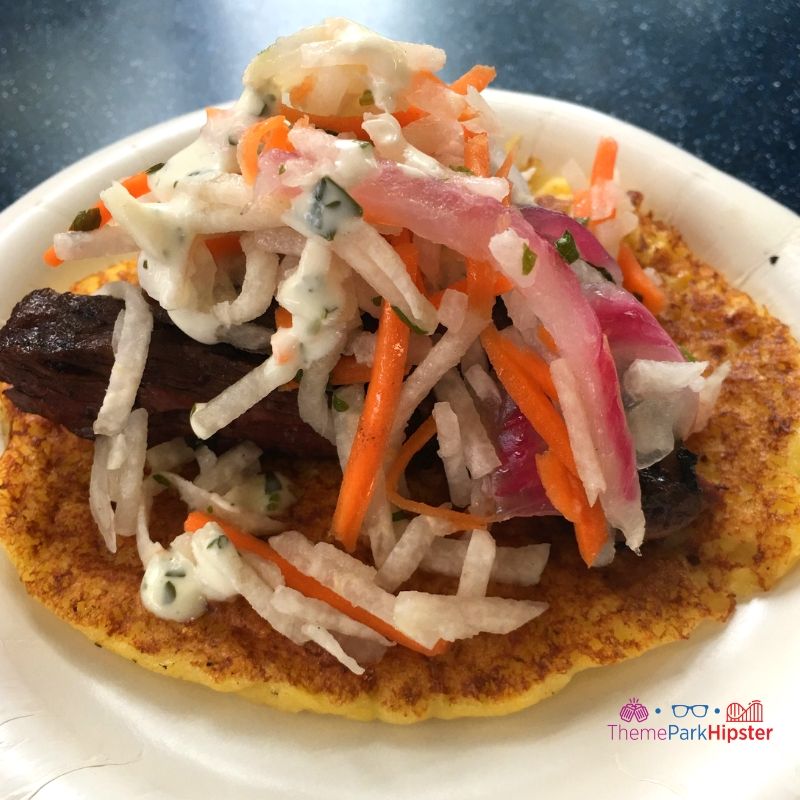 Charred Chimichurri Skirt Steak on a smoked corn cake with pickled vegetable slaw and cilantro aioli at Flavors from Fire Epcot. Keep reading to get the best Epcot Food and Wine Festival Tips!