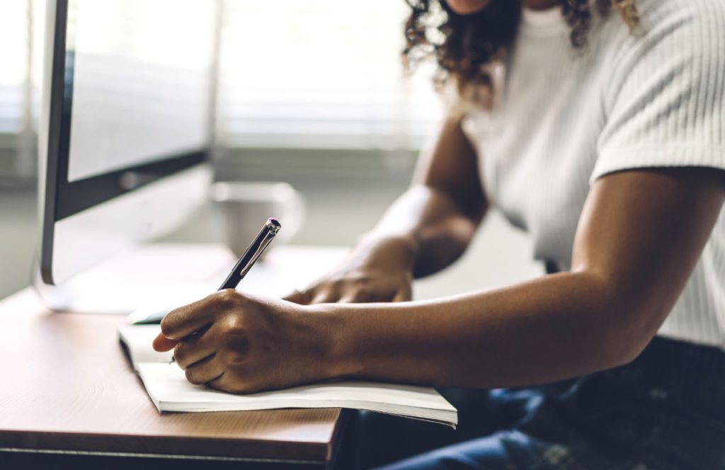 Black Lady on Computer writing down travel insurance quotes.