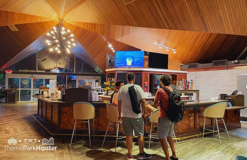 Springs Taproom bar during Busch Gardens Tampa Food and Wine Festival with guests standing at the bar with hanging spherical lights above. Keep reading to learn more about what to eat at Busch Gardens Tampa.