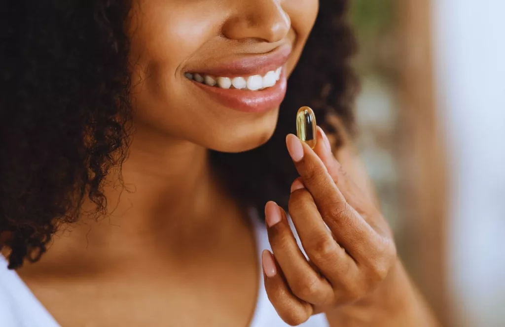 Black Woman Taking Vitamin to stay healthy on vacation. Keep reading to learn how to deal with traveling alone with anxiety on your solo trip