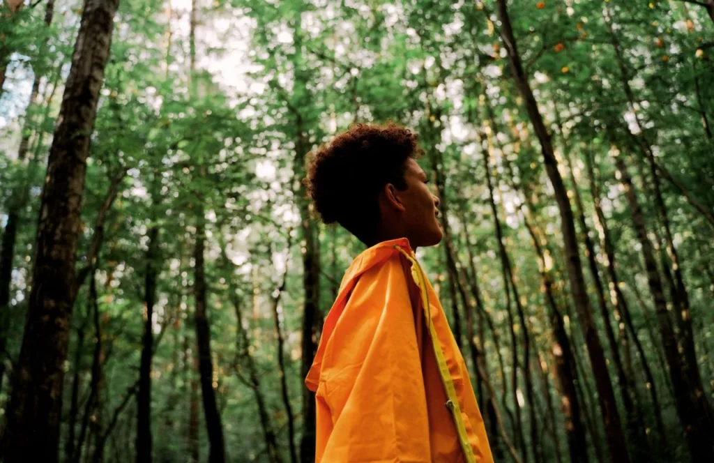 Black woman walking through a lush forest on vacation. Keep reading to learn how to deal with traveling alone with anxiety on your solo trip