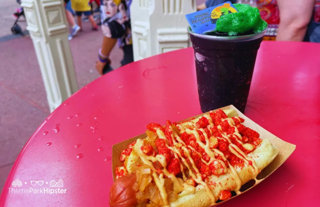 Mickey's Not So Scary Halloween Party Food at Disney Magic Kingdom Theme Park Hocus Pocus Sanderson Sisters Black and Green Drink with Hotdog Topped with onions firehot cheetos and sauce at Casey's Corner. One of the best restaurants at Walt Disney World.