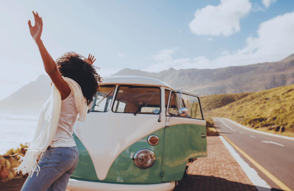 Woman having fun on the side of the road in front of her van while listening to one of the best audiobooks for solo road trips