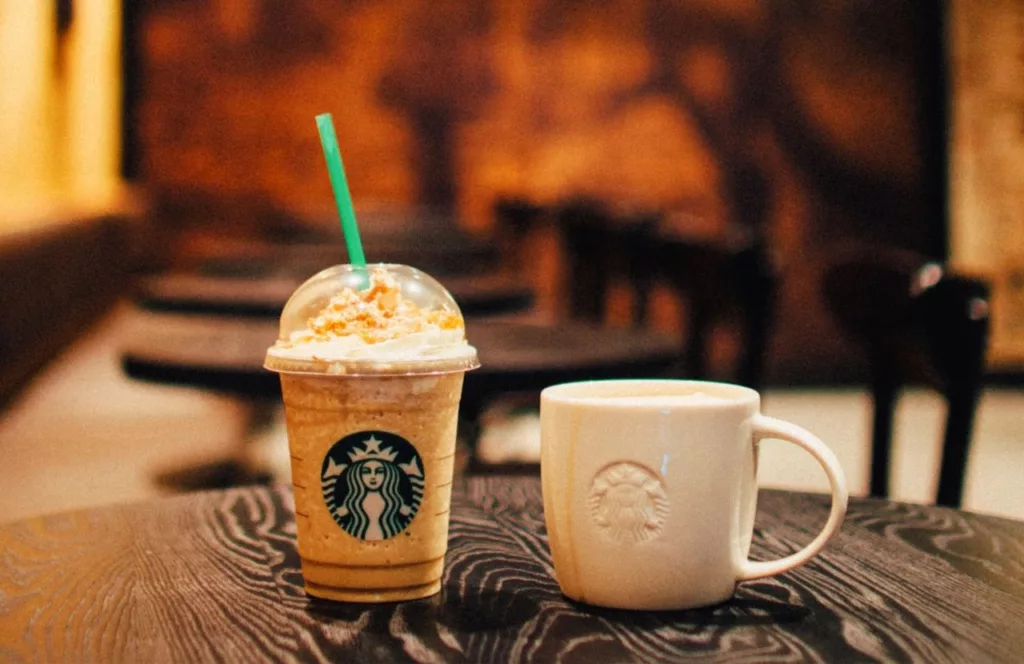 Hershey Tanger Outlets Starbucks Coffee with whipped topping and a starbucks mug beside it on a rustic inspired table. Keep reading to find out more about the best things to do near Hersheypark.